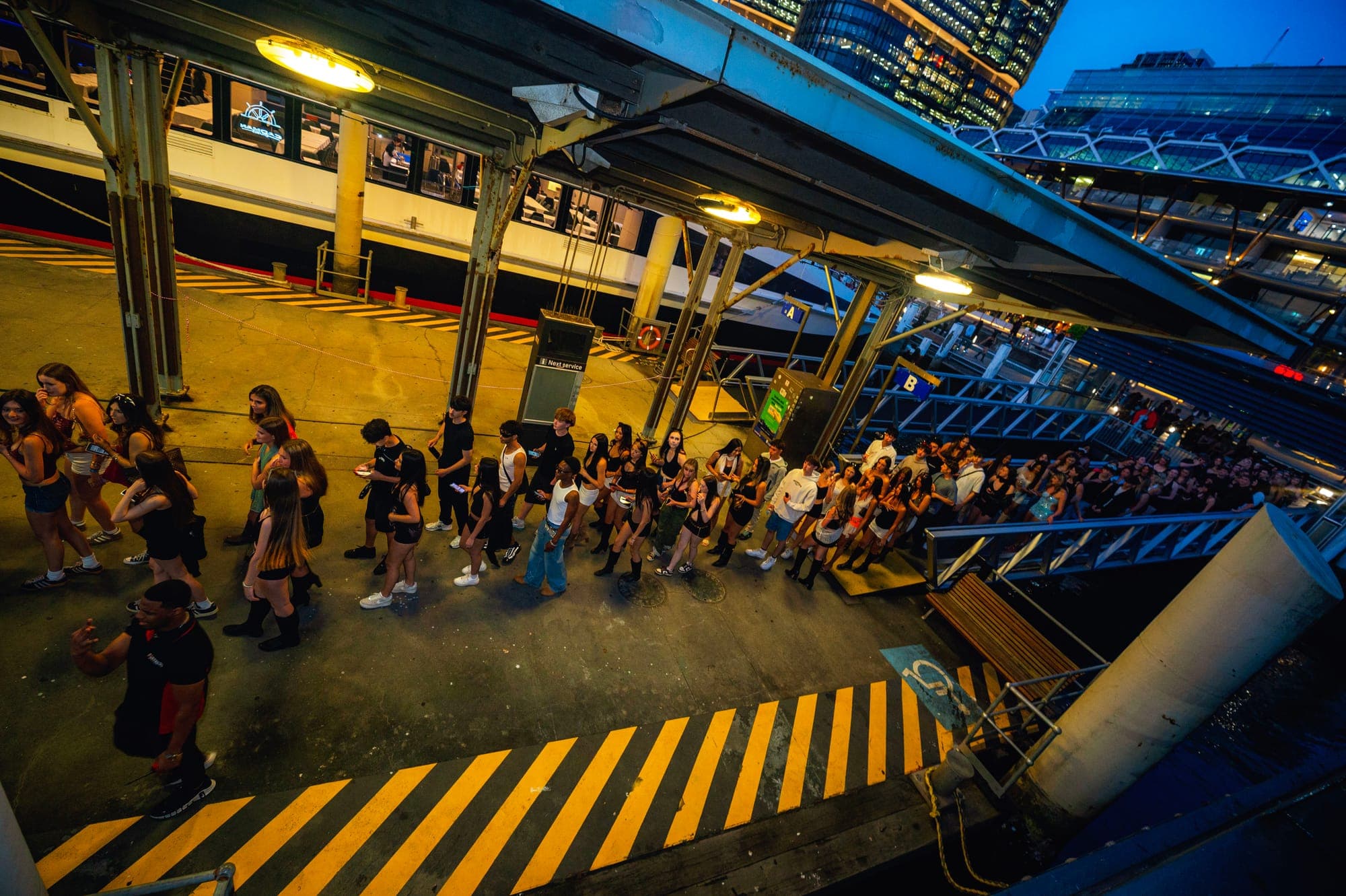 Guests lining up along the wharf at dusk to board a Vex U18s boat party