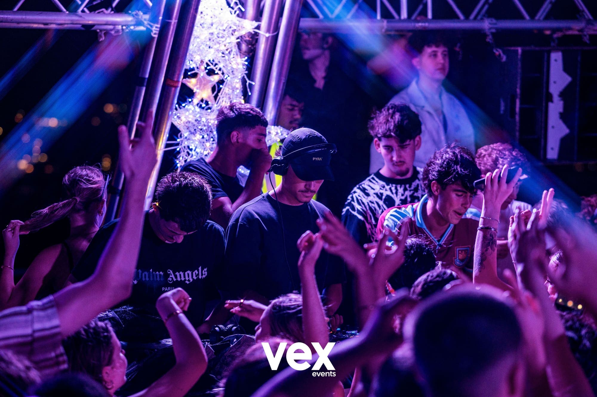 A DJ in headphones playing under a lighting rig washing the crowd in blue and purple