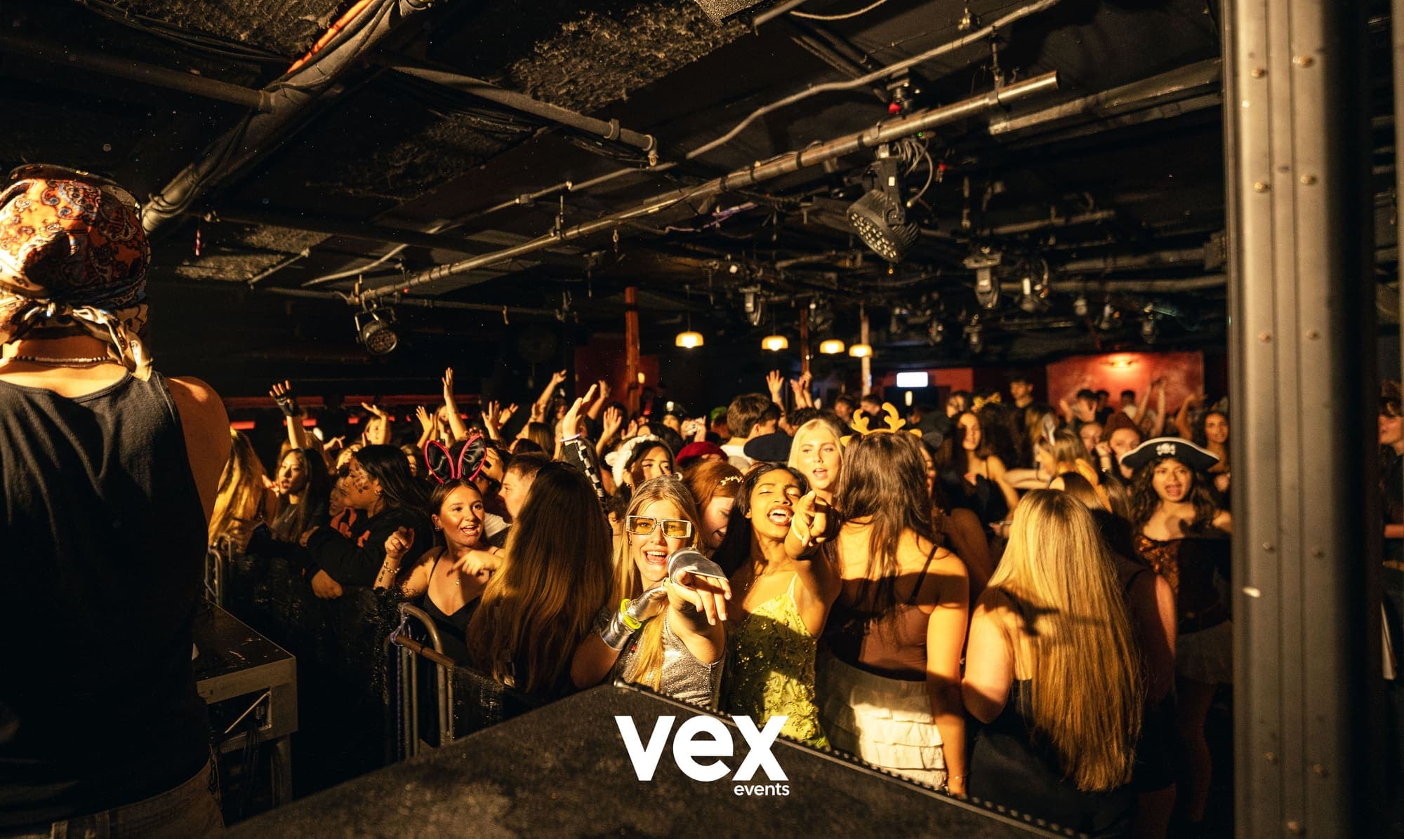 A full venue floor seen from behind the booth, lit warm, with the crowd pressed towards the front